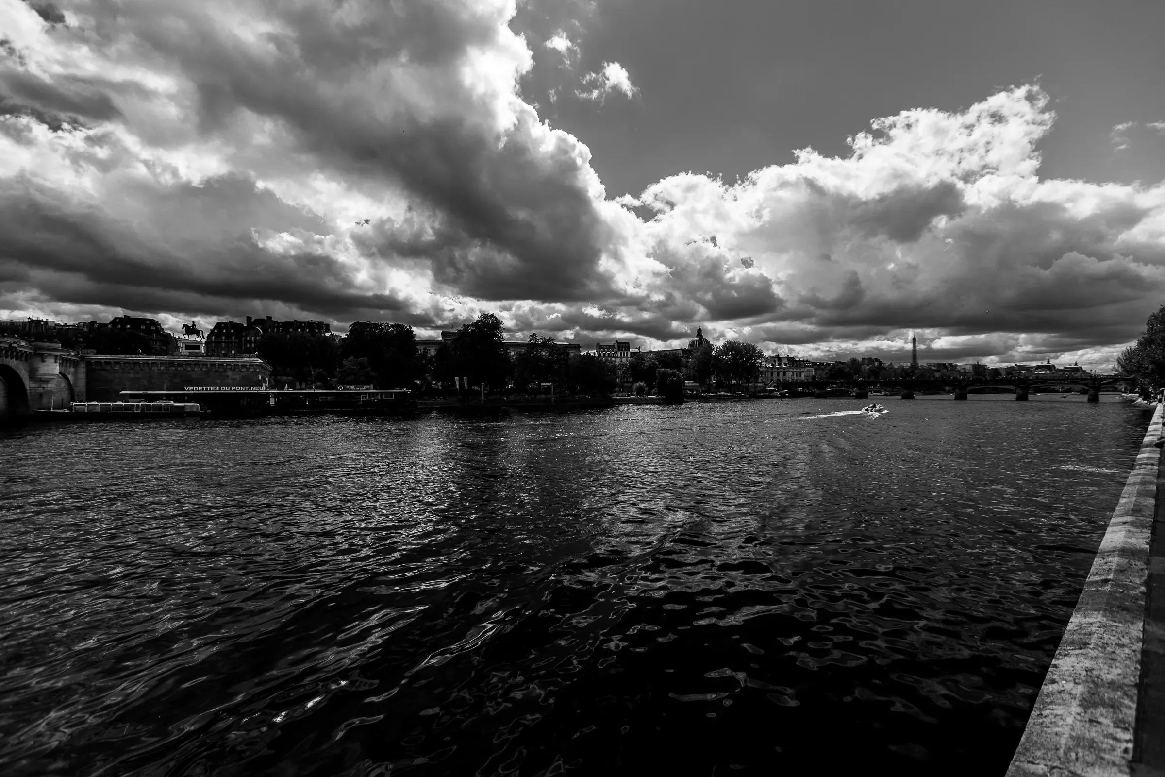 River Seine with the Eiffel Tower as a tiny silhouette on the right horizon, brooding storm clouds filling the wide sky, the quai wall in shadow