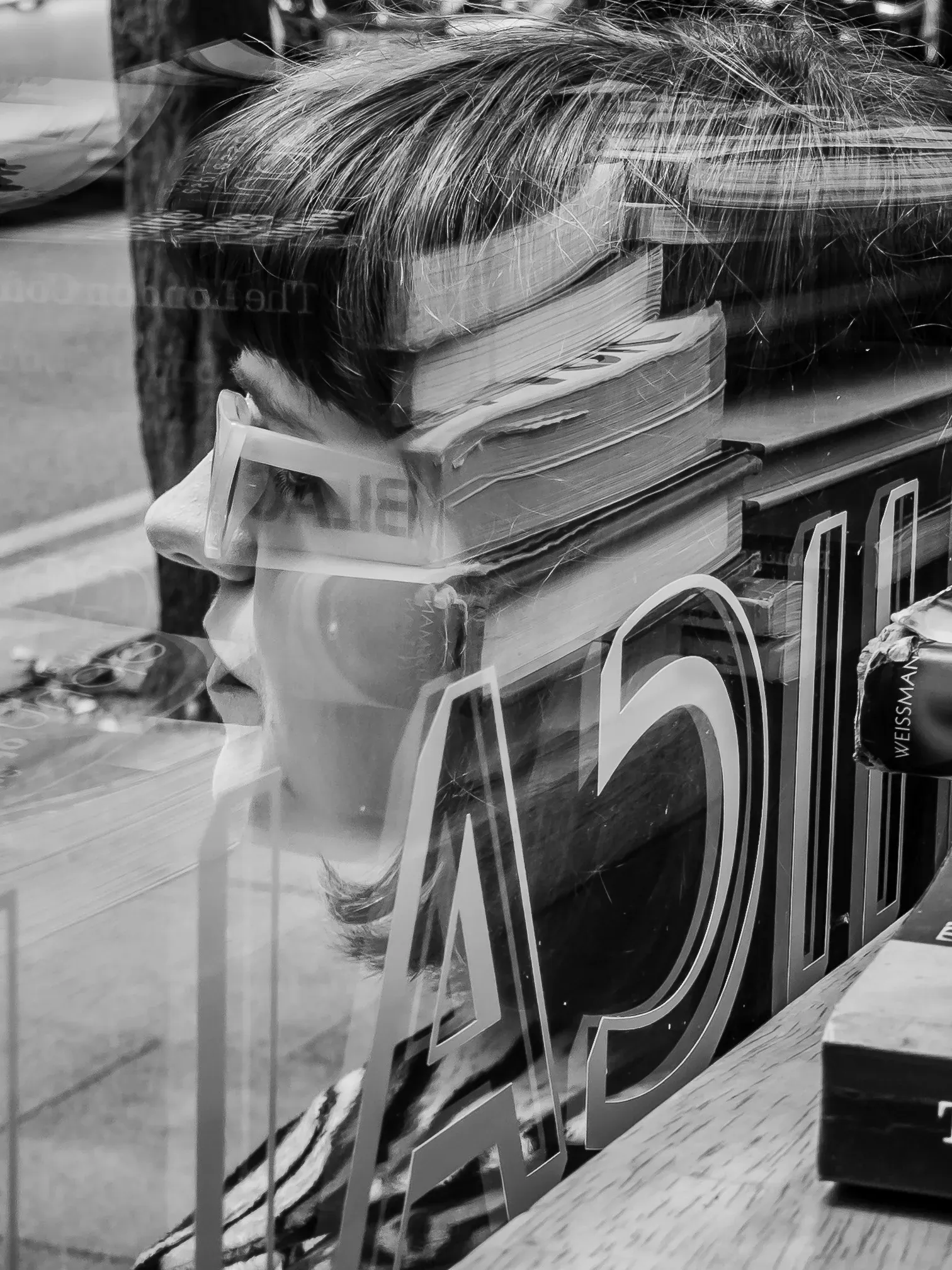 Double-exposure-style reflection of a mannequin's head wearing sunglasses, overlaid with book spines and shop lettering in a window display