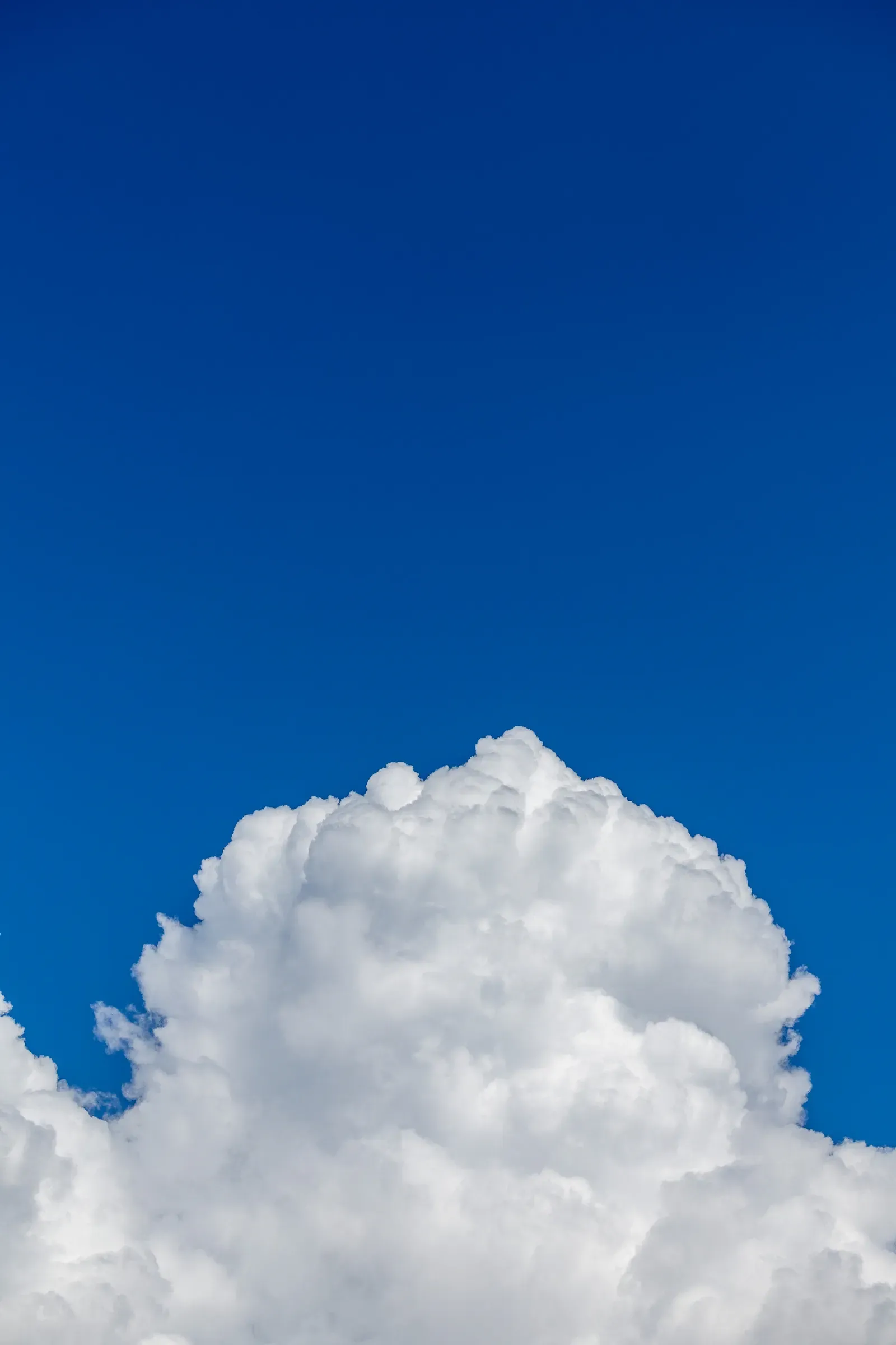 A single white cumulus cloud billowing up from the bottom of the frame against a deep blue sky, no ground visible