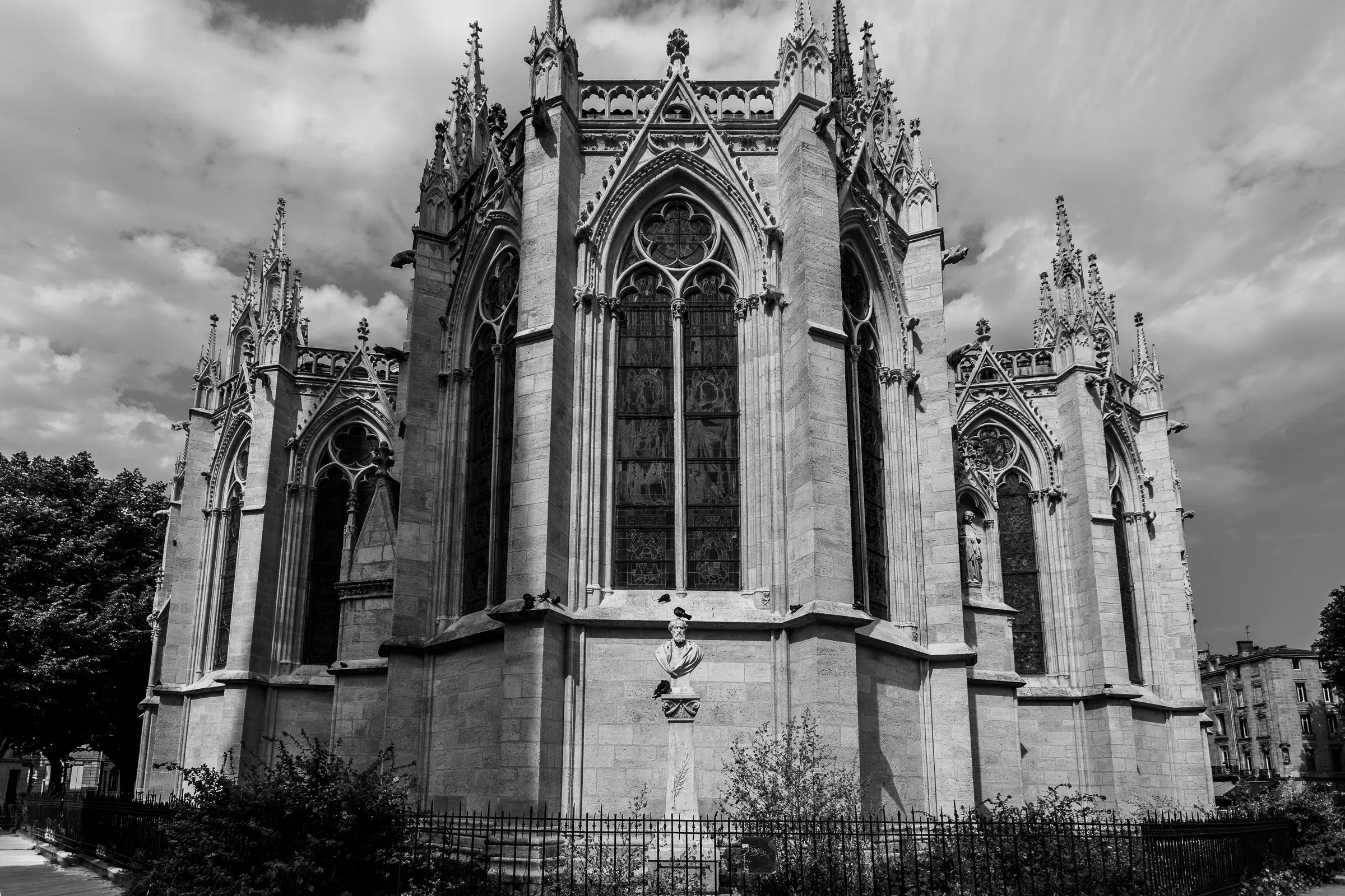 Gothic apse of a cathedral with tall lancet windows, flying buttresses, and pinnacles against a cloudy sky, ivy at the base