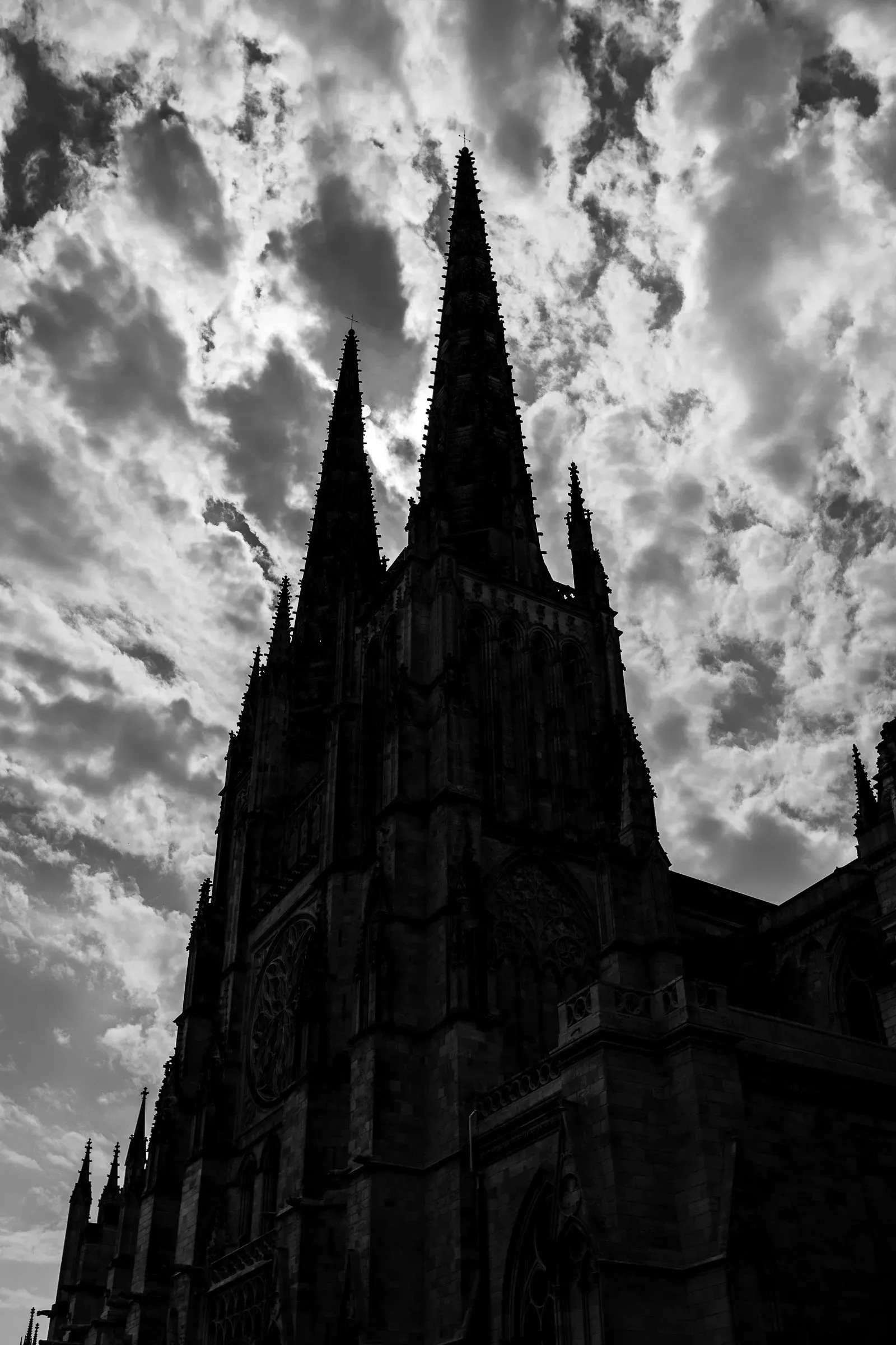 Gothic cathedral twin spires and facade in near-silhouette against a turbulent sky, every carved detail swallowed by shadow