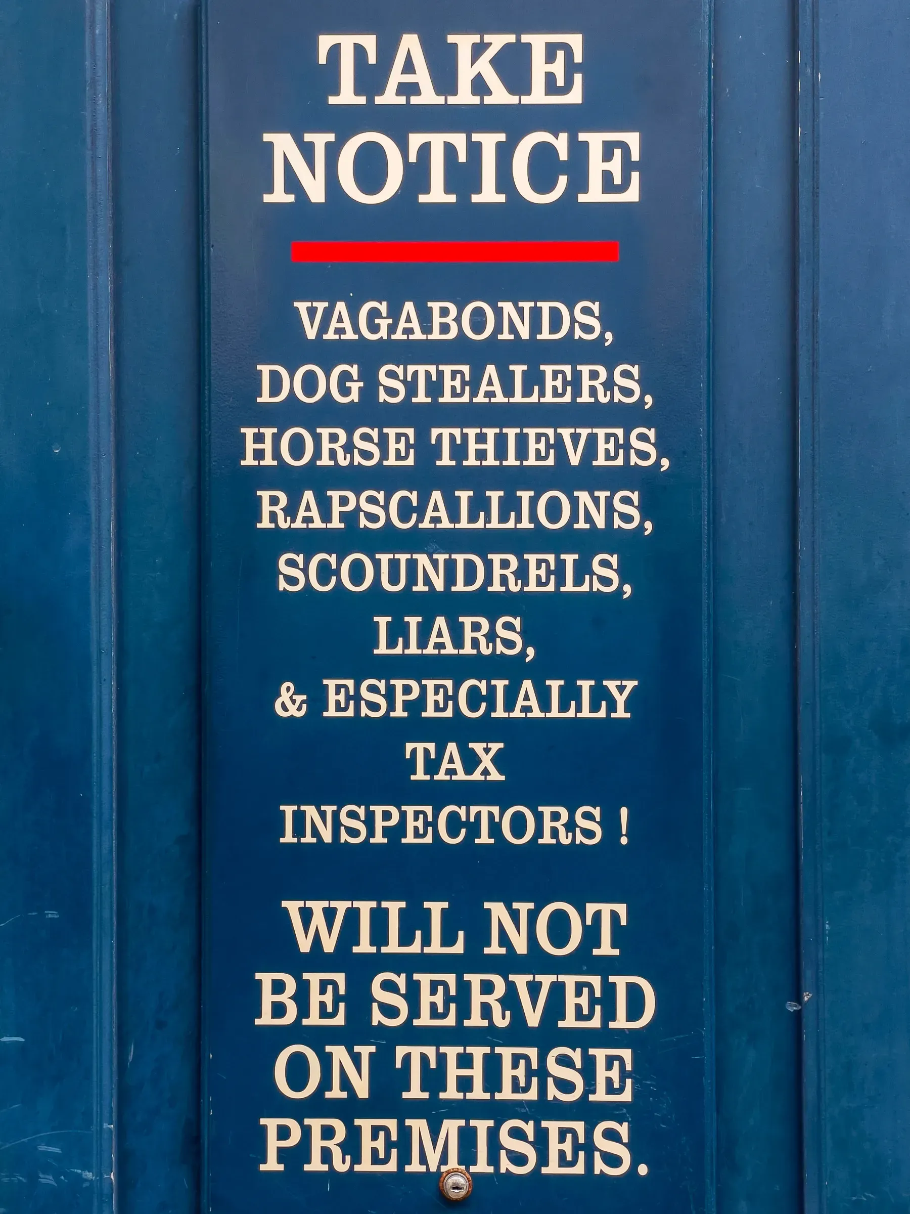 Blue painted door with white serif text listing vagabonds, dog stealers, horse thieves, rapscallions, scoundrels, liars, and especially tax inspectors as unwelcome on the premises