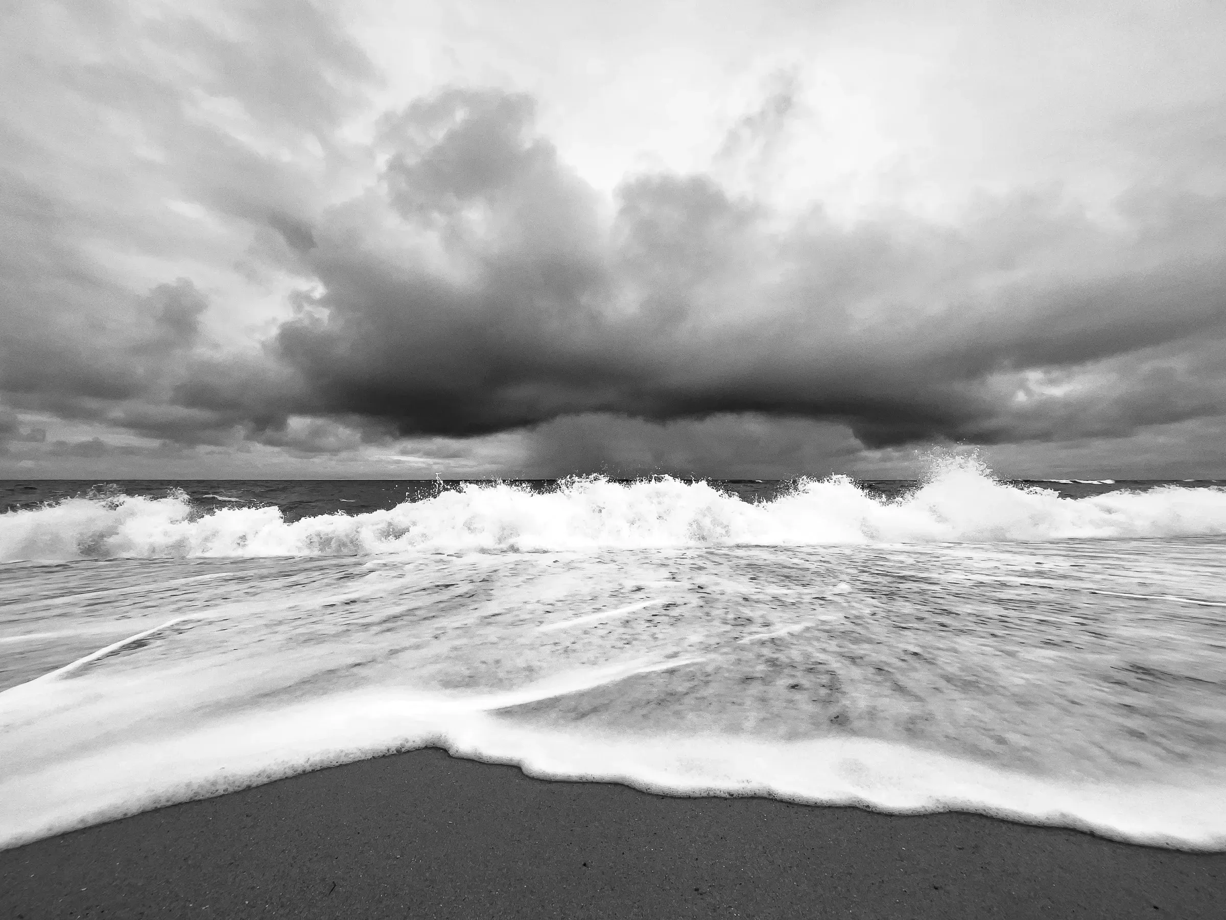 Wide angle view from beach level as a large wave breaks and foams across the sand, storm clouds building on the horizon over the sea
