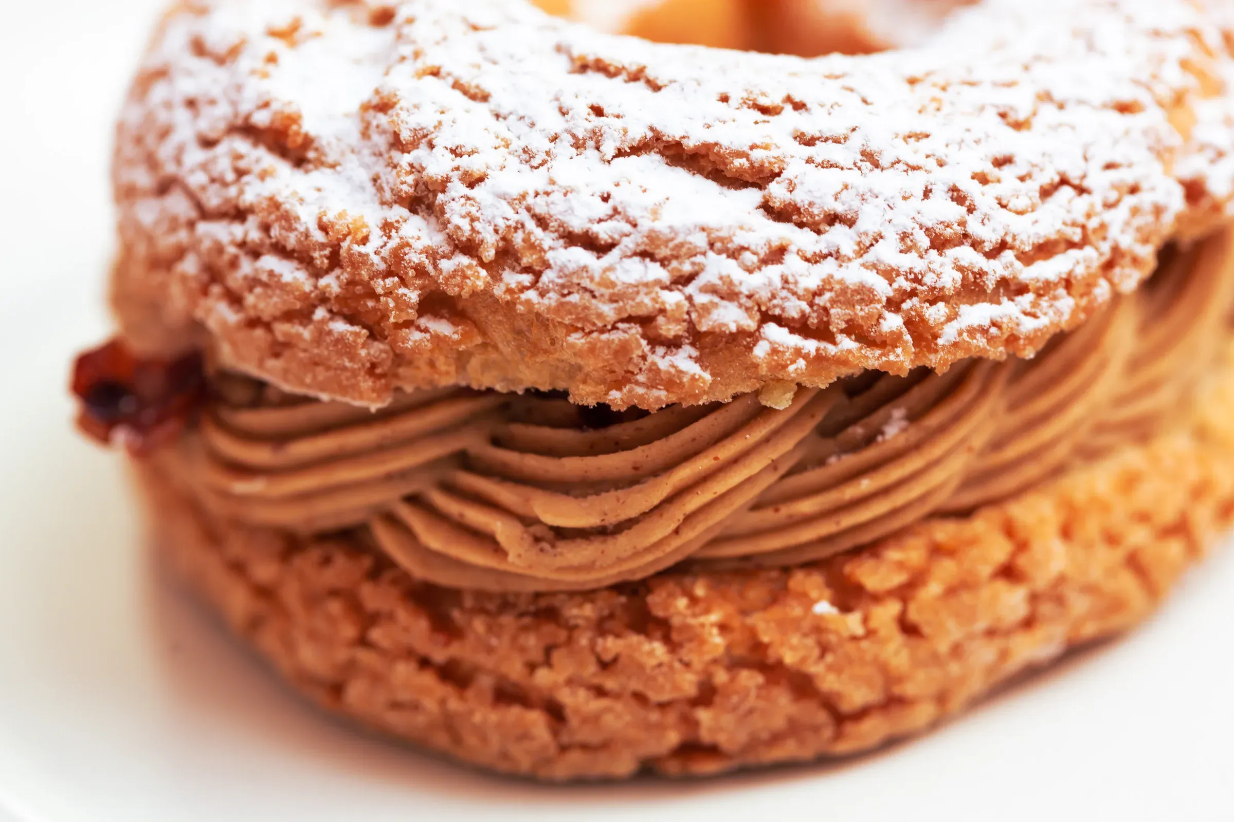 Paris-Brest whole on a white plate — choux ring with praline mousseline cream piped in ridges, powdered sugar on top