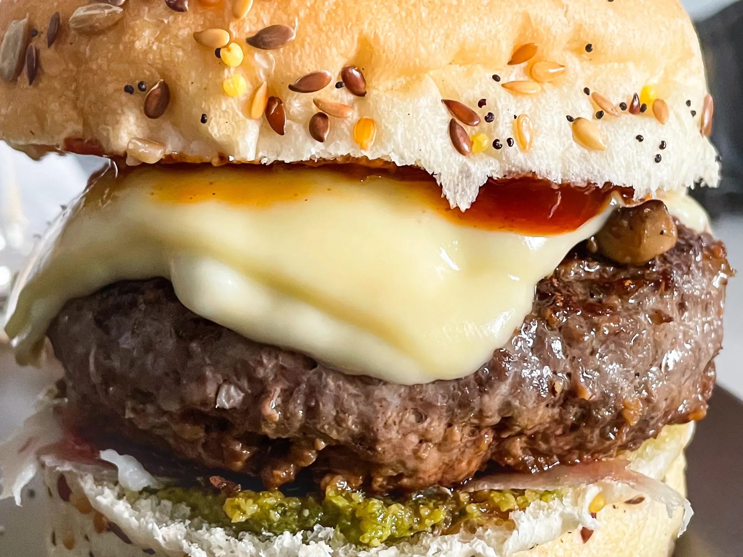 Cheeseburger close-up cross-section — seeded bun, melted white cheese draped over a beef patty, mustard and pickles below