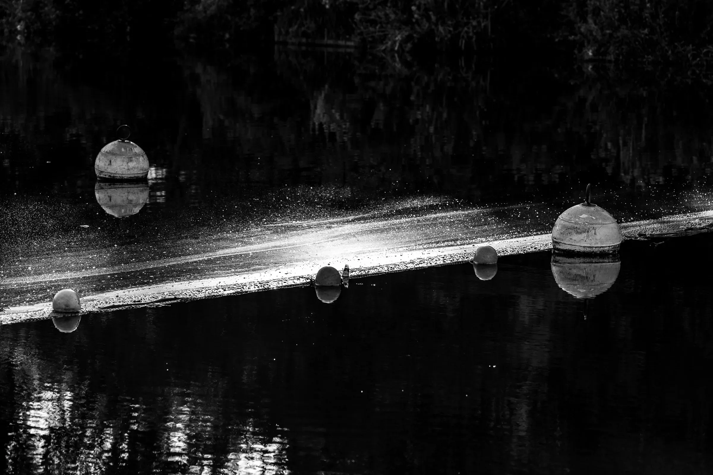 Several spherical buoys floating on dark still water, a diagonal streak of reflected light cutting across the scene