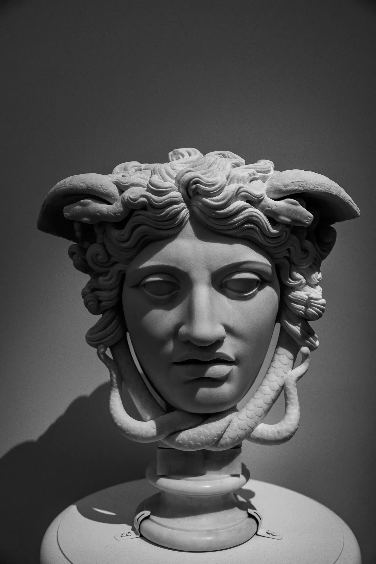 Marble museum bust of a mythological figure — ram horns curving from the temples, a serpent coiling around the neck, direct gaze