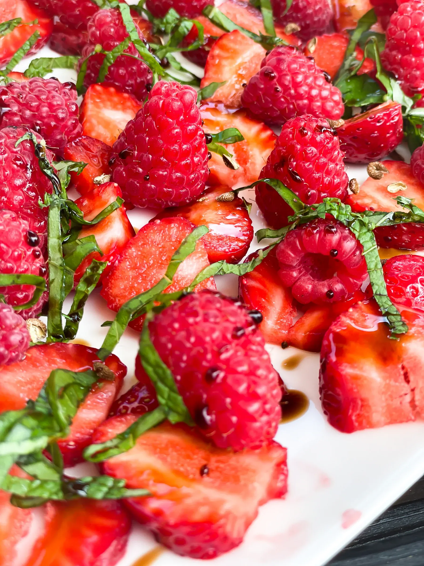 Strawberry and raspberry salad with chiffonade of fresh mint and a balsamic reduction drizzle on a white plate