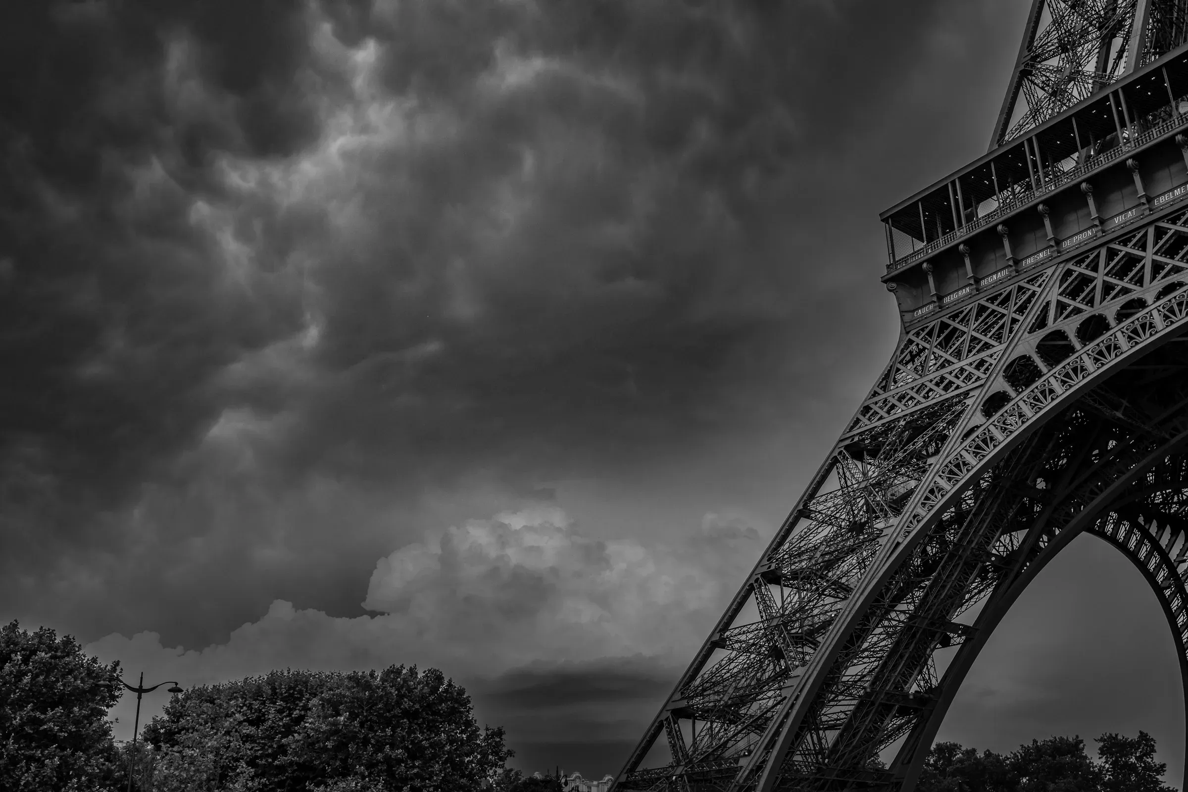 Eiffel tower, cut to one of its feet, with a dark cloudy sky in the background, forecast to a huge storm