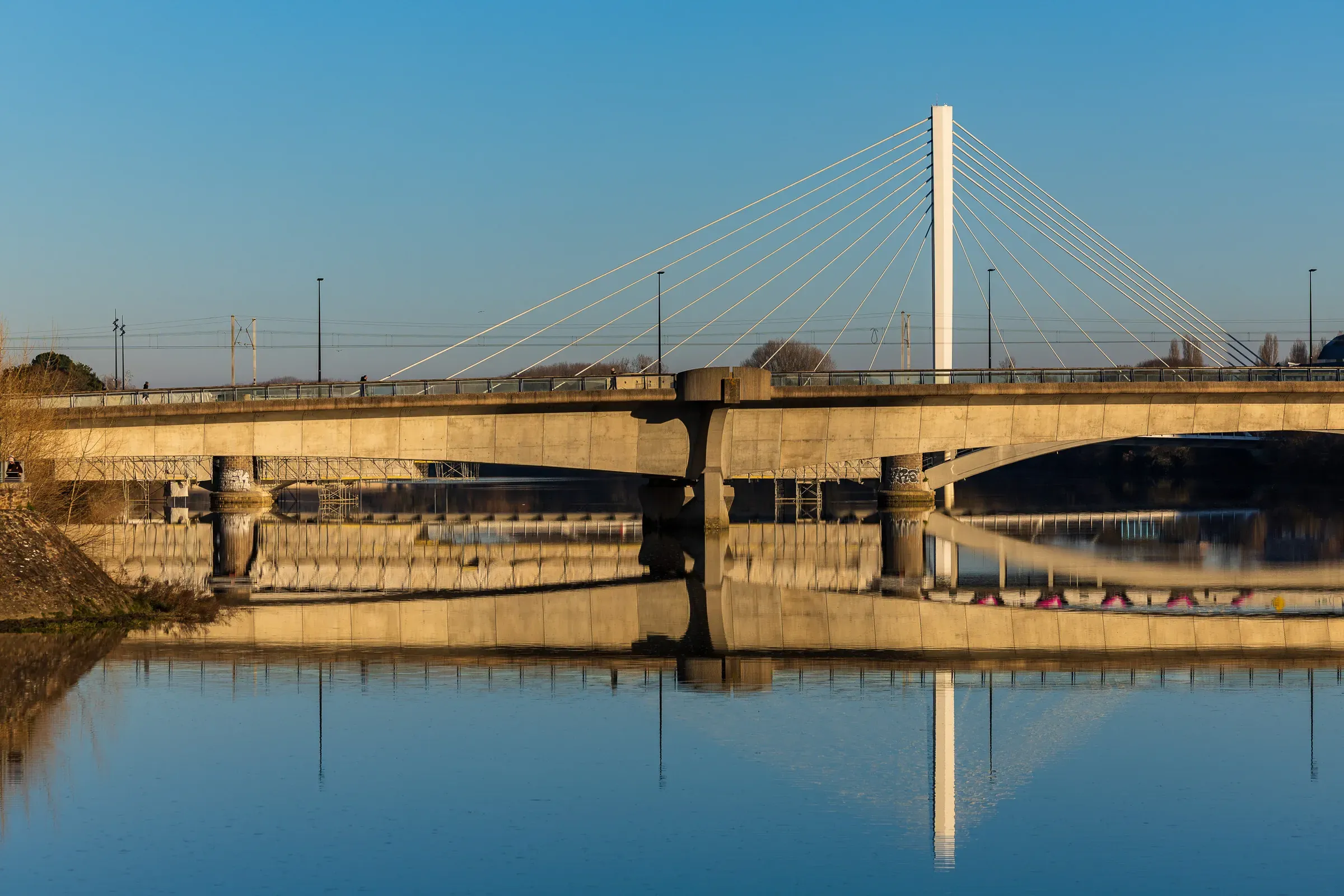 A concrete cable-stayed bridge reflected perfectly in the still blue Loire, clear winter sky