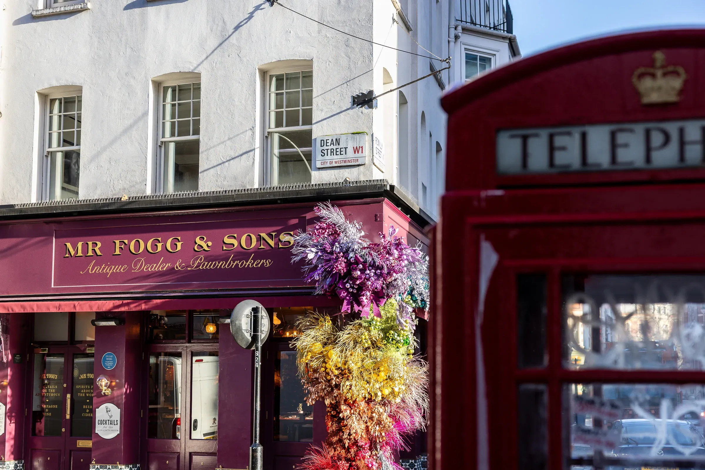 Mr Fogg & Sons antique dealer on Dean Street, a rainbow flower display bursting from the doorway, a red phone box in the foreground, Soho, London