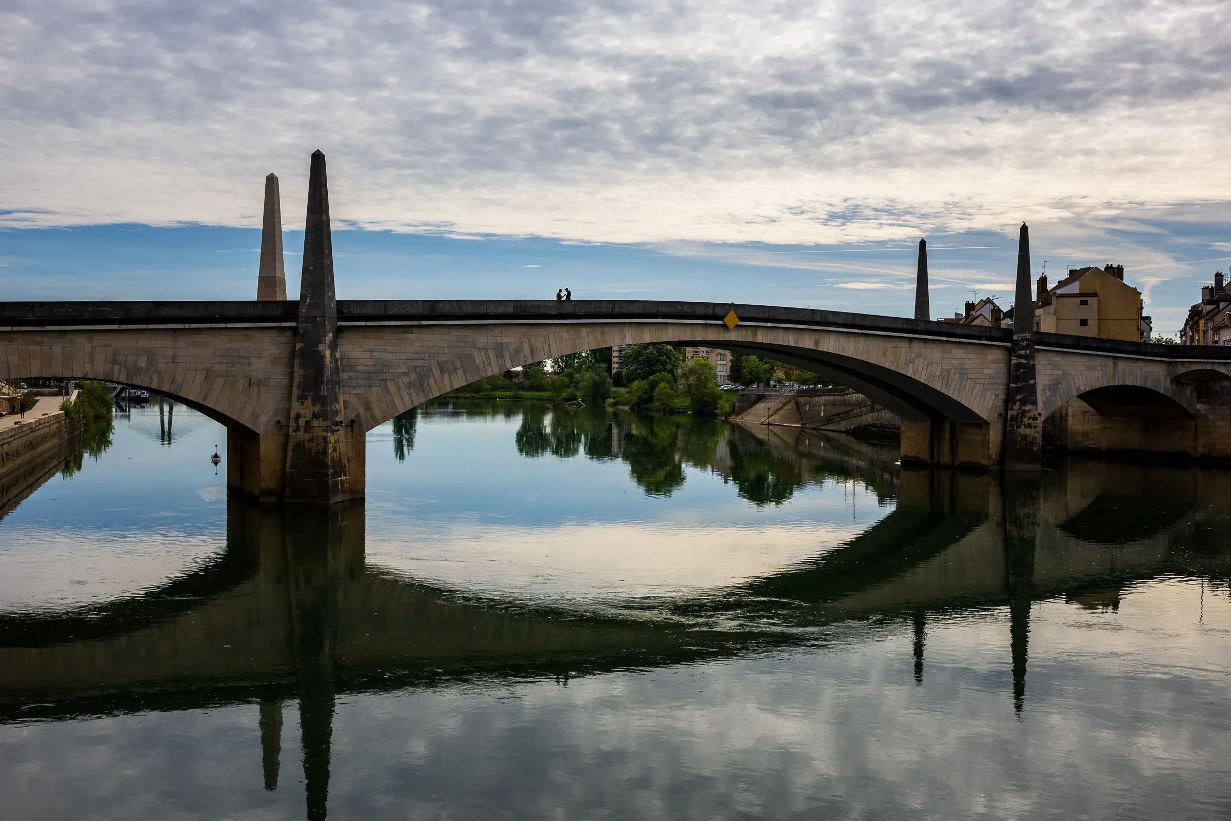 Stone arch bridge over the Saône with twin obelisks, a domed building and bell tower behind, calm reflections, Chalon-sur-Saône