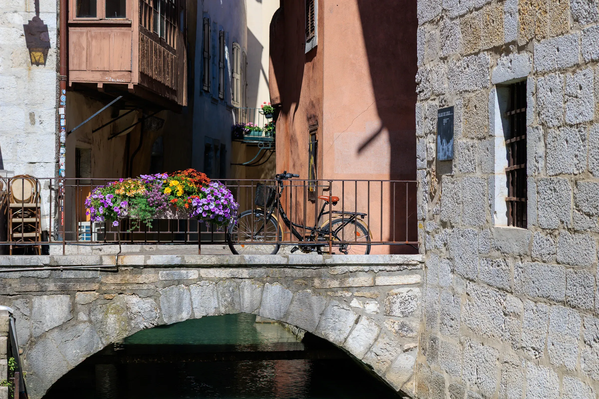 Bicycle parked on a stone bridge over a canal with colorful flowers, Annecy old town